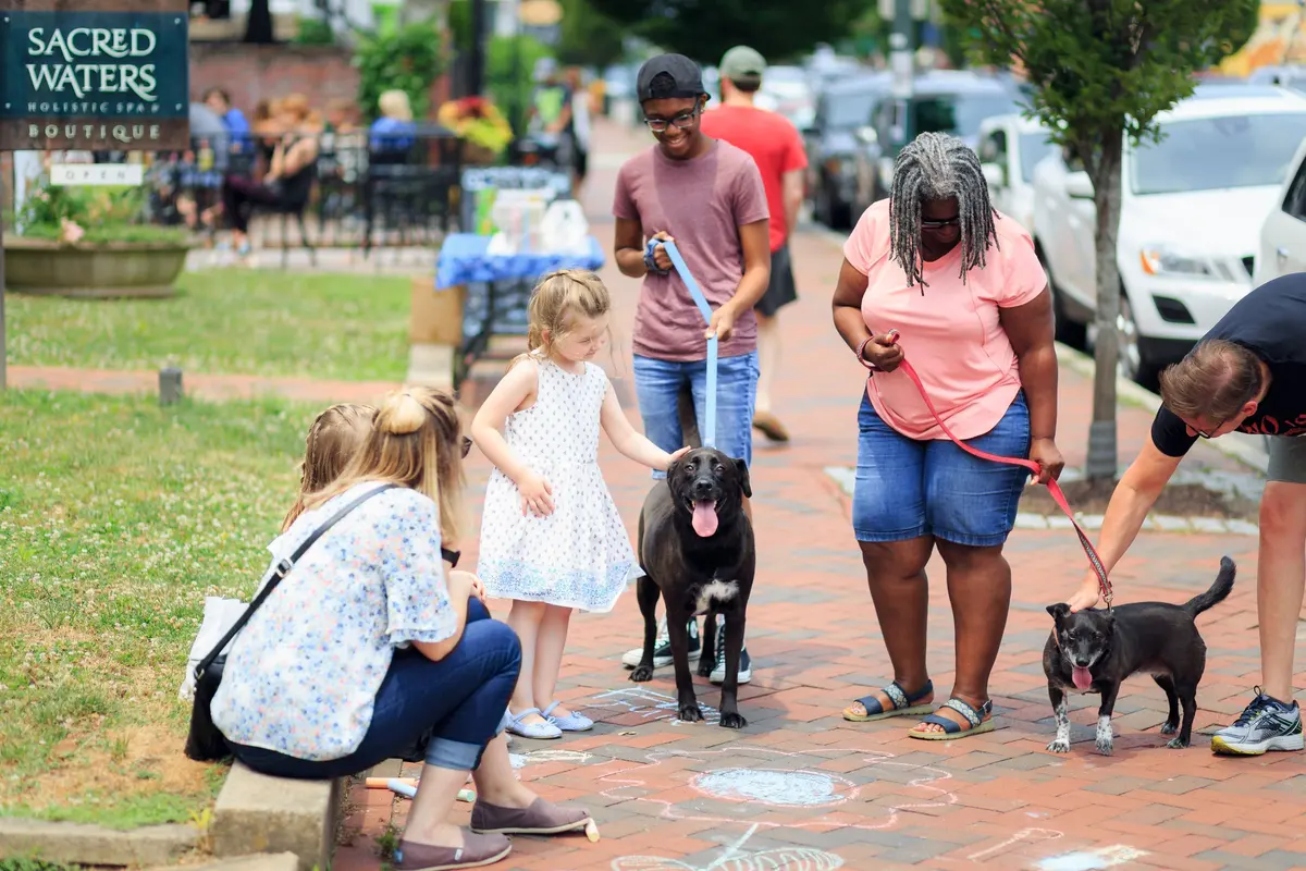 Adults and children sit together on the grass in a park with a dog.